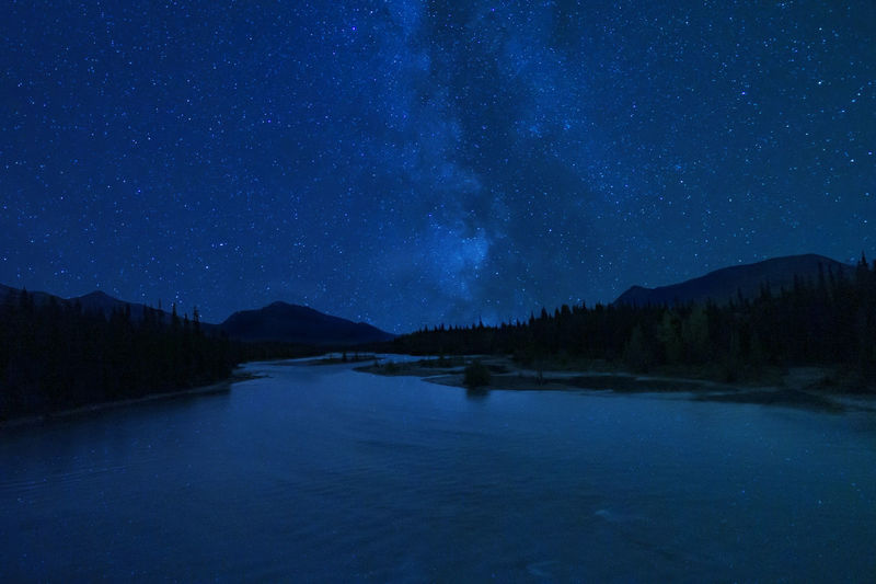 Stunning milky way night stars over mountain wilderness river pine trees