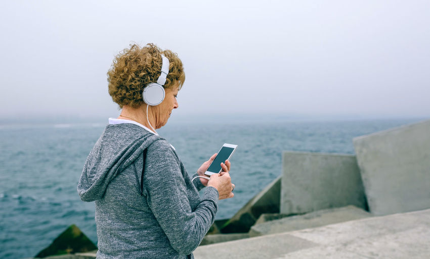 Woman using mobile phone while standing at beach against sky