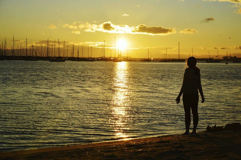Rear view of silhouette woman standing at st kilda beach during sunset