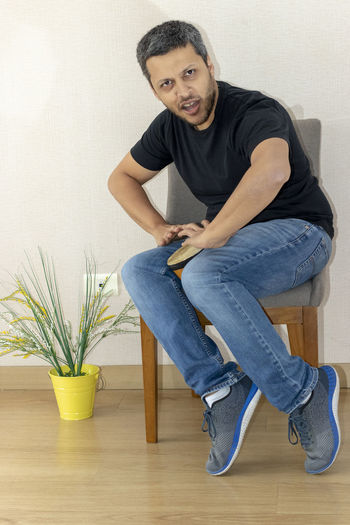 Portrait of man playing drum while sitting on chair against wall at home