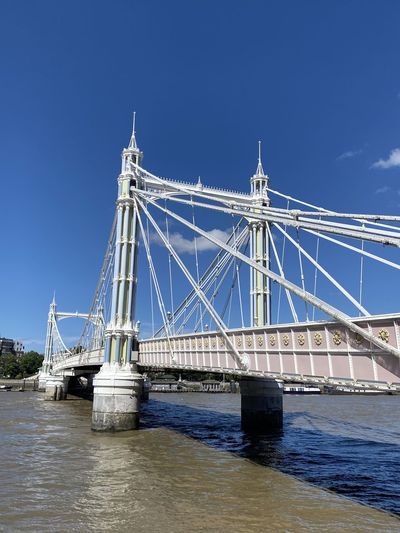Low angle view of suspension bridge over river against blue sky