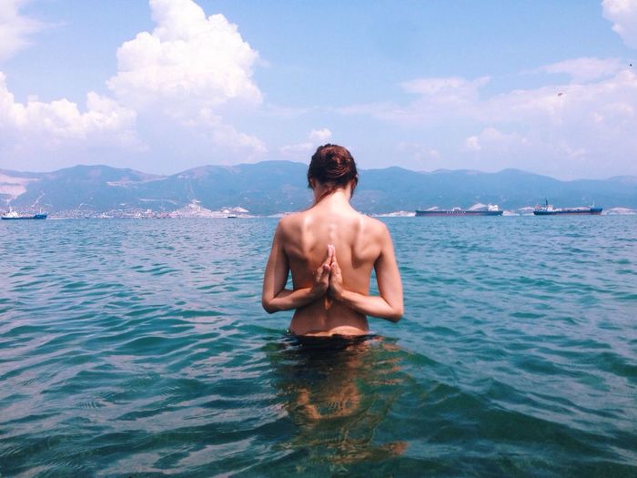 Rear view of shirtless woman exercising yoga in sea against sky