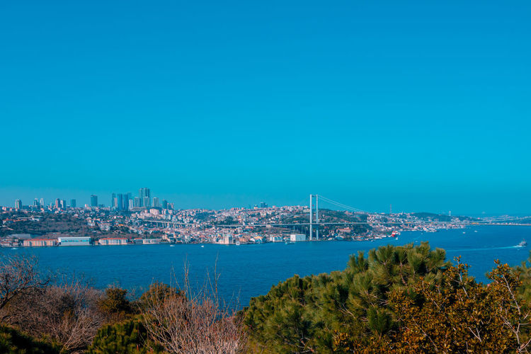 Panoramic view of city by sea against clear blue sky