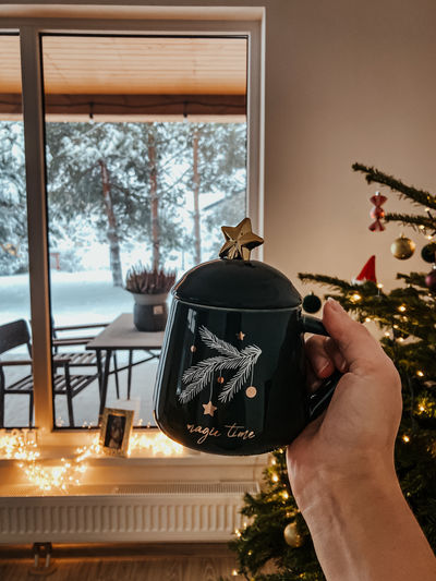 Hand holding a christmas mug in front of a tree