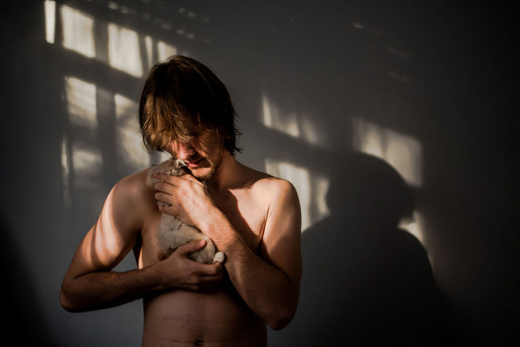 Close-up of shirtless young man carrying dog against wall