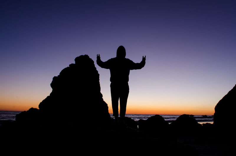 Silhouette man standing on cliff against clear sky during sunset