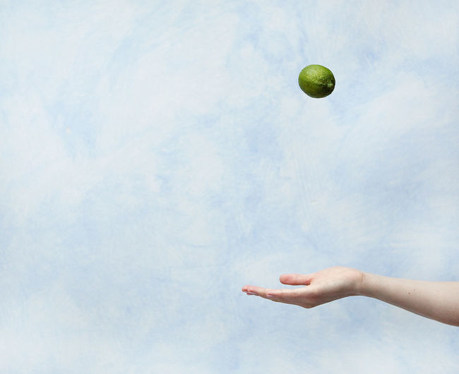Close-up of hand holding ball in mid-air against sky
