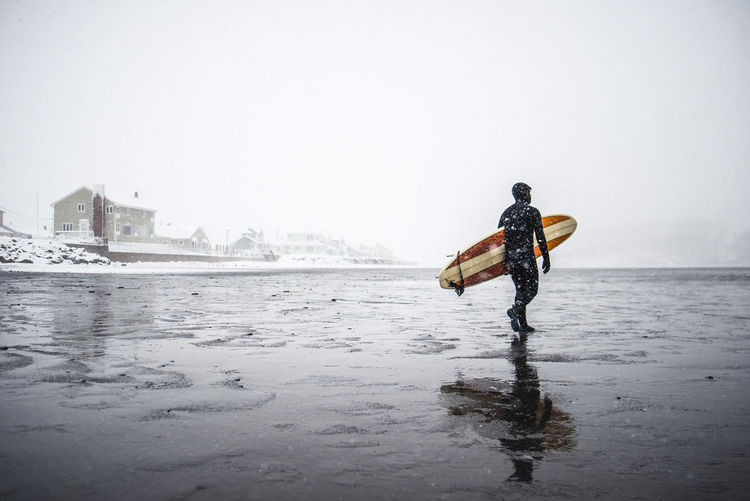 Surfer walks along maine beach during winter snow storm
