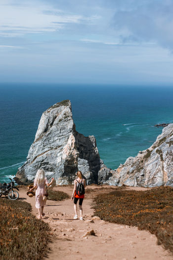 Rear view of people walking on rock by sea against sky