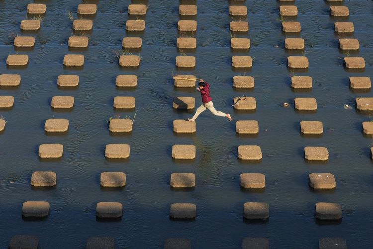 High angle view of man crossing concrete blocks in lake