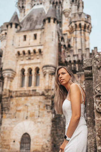 Young woman looking away while standing against historic building