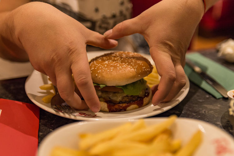 Close-up of hands picking burger from plate