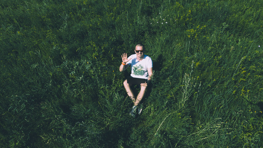 Full length of smiling man sitting amidst grass