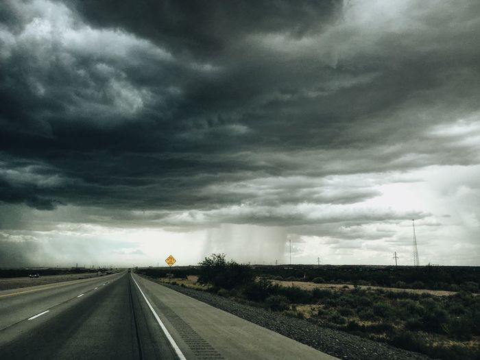 Road passing through landscape against storm clouds