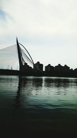 Silhouette bridge over river against sky in city
