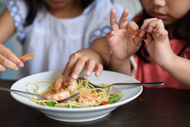Close-up of sisters eating prawn noodles in plate at table
