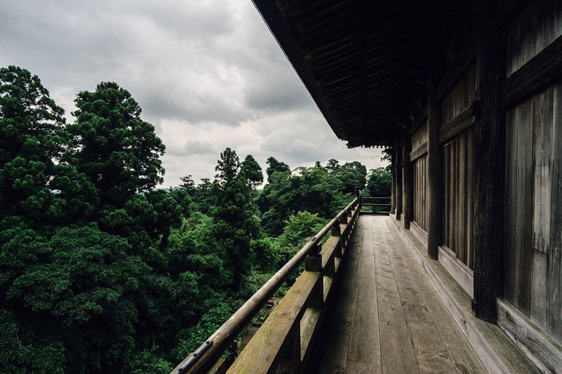 Empty balcony of japanese temple by trees against cloudy sky