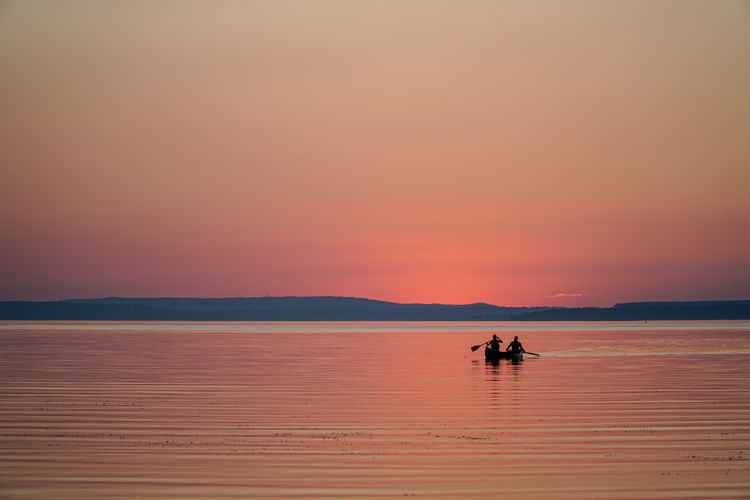 Silhouette people on boat in sea against orange sky