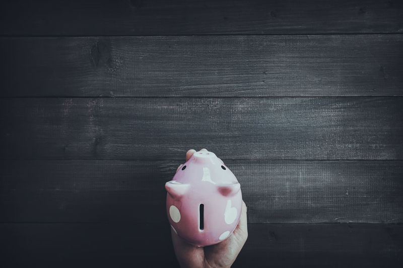 Close-up of hands holding pink piggy bank at table
