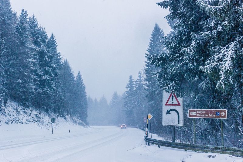 Road by snow covered landscape against sky