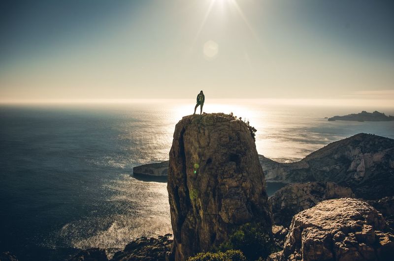Man standing on rock by sea against sky