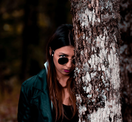 Portrait of young woman wearing sunglasses against tree trunk