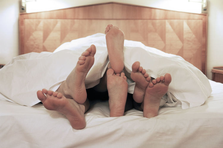 Three people under blanket on bed