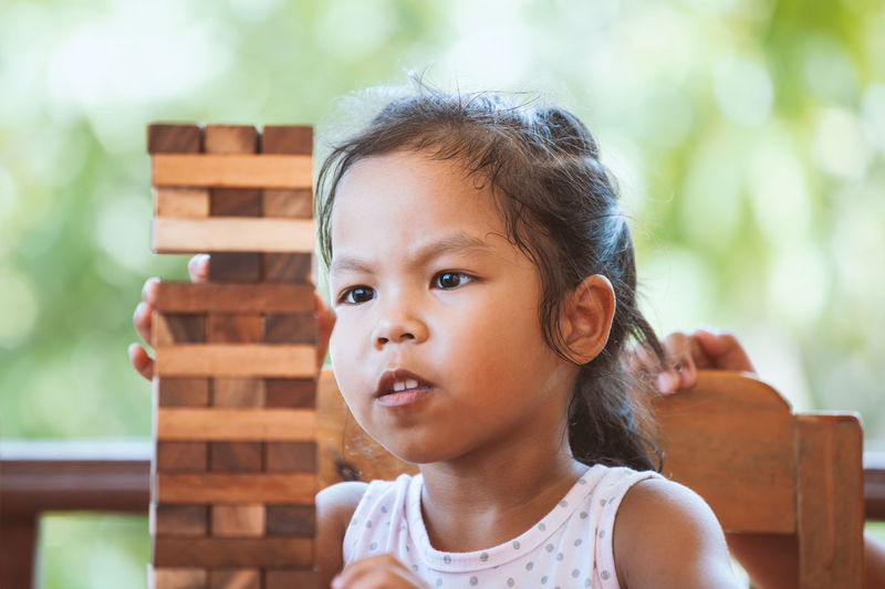 Girl playing with wooden toy blocks while sitting in porch