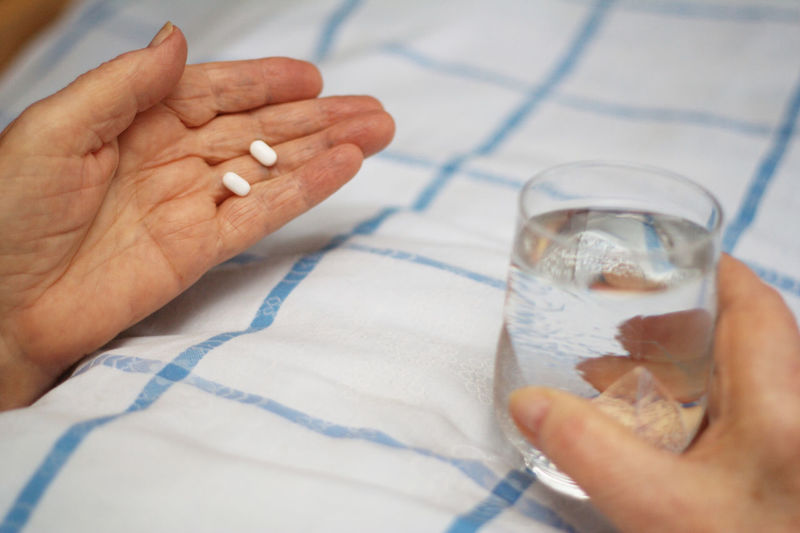 Cropped hands holding pills and glass of water