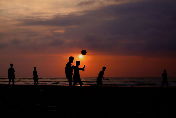 Silhouette people playing on beach against sky during sunset