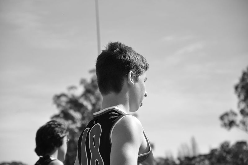 Teenage boy wearing sports uniform standing against sky