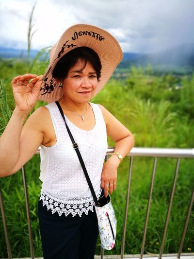 Portrait of woman in hat standing by railing against plants