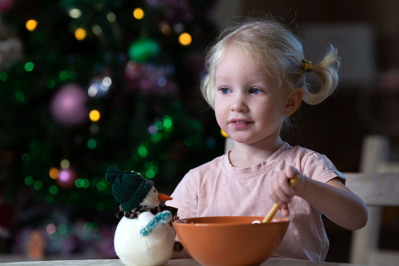 Cute blond toddler girl with blue eyes having her meal in new year entourage. girl is left-handed.