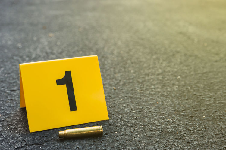 A single brass bullet shell casing laying on the ground next to a crime scene evidence marker