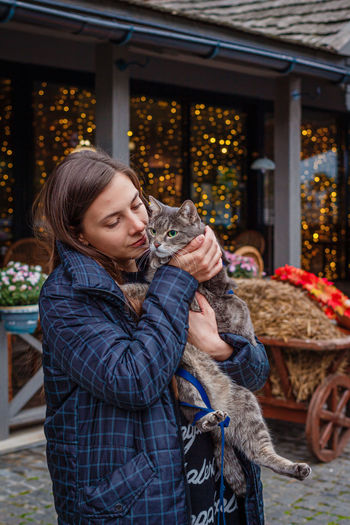 Young woman holding cat against store