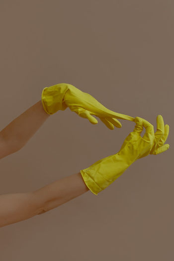 Cropped hands of person removing yellow gloves against beige background
