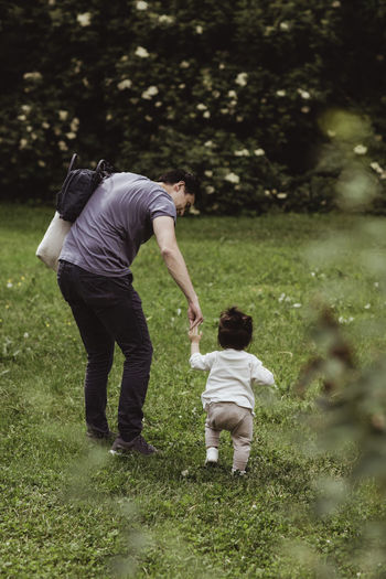 Father helping baby son to walk on grass in park