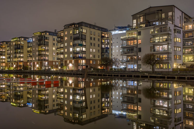 Illuminated buildings by river against sky in city at night