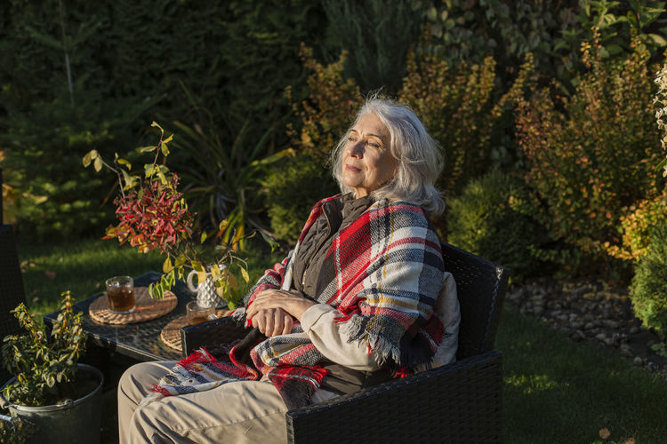 Senior woman sitting in autumn garden in an armchair