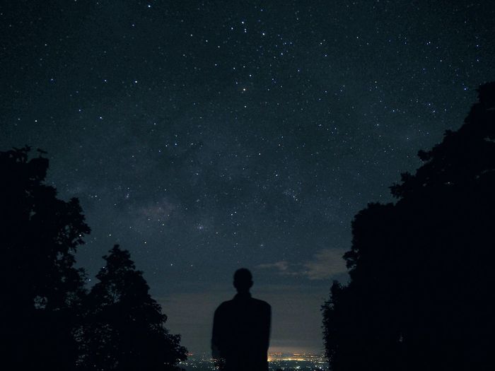 Rear view of silhouette person standing against star field at night