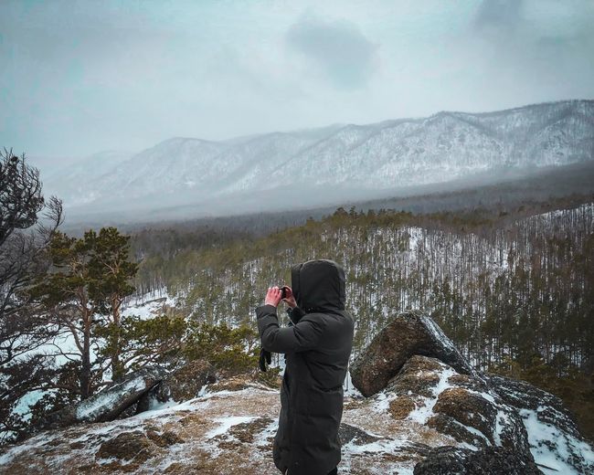 Man photographing on mountain against sky during winter