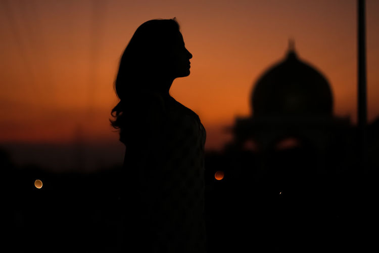 Side view of silhouette woman standing against sky during sunset