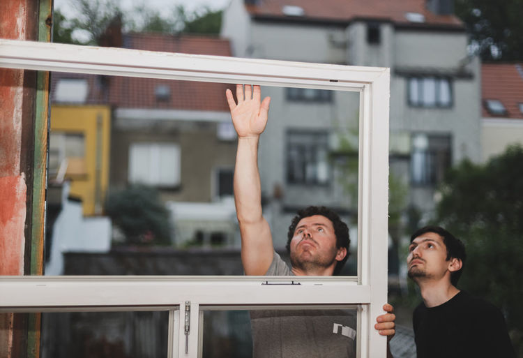 Two caucasian male builders inspects dirty window frames.