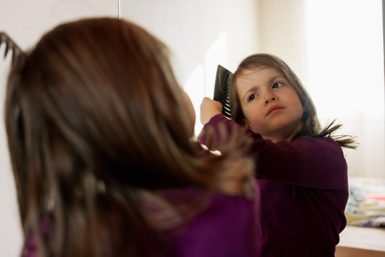 Child combing her hair in front of mirror at home