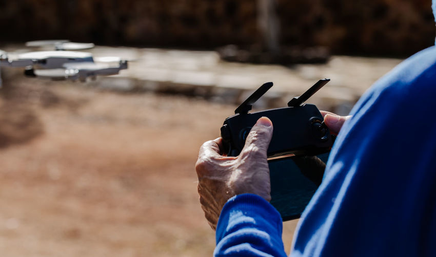 Rear view of the elderly man piloting the drone looking at the remote control display while standing