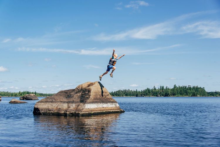 Man jumping over lake against sky