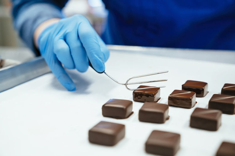 Midsection of chef holding chocolate dipped with fork in tray