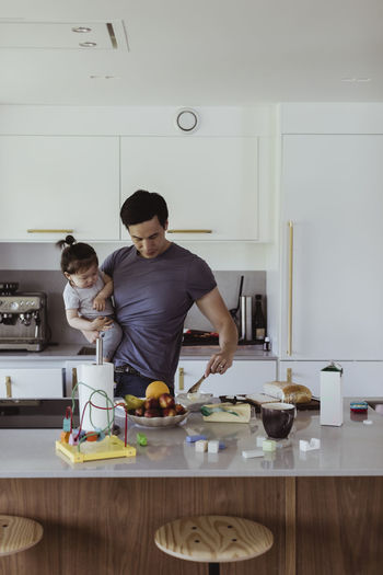 Father carrying baby son while preparing food in kitchen