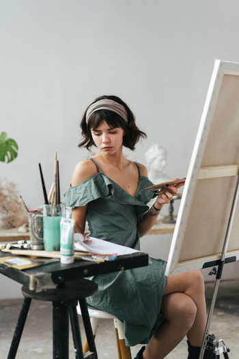 Young woman painting on canvas while sitting on table