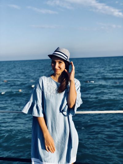 Portrait of woman wearing hat standing against sea